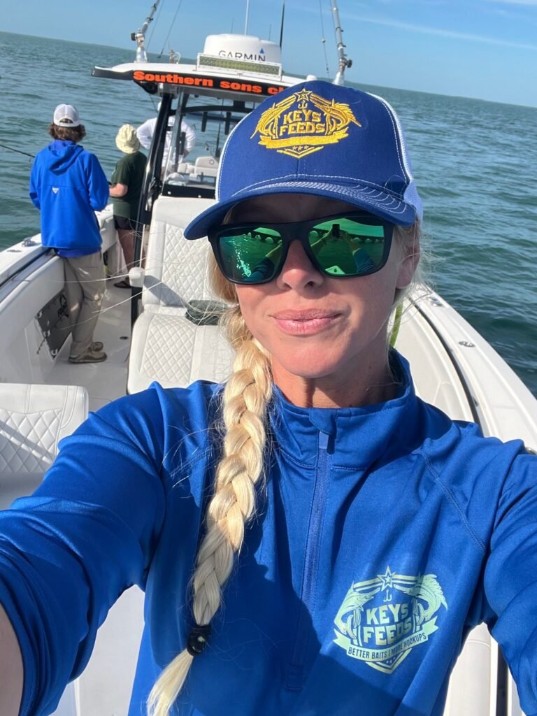 Angler wearing Keys Feeds hat and shirt aboard fishing boat using premium live bait fish food for pilchards and goggle eyes