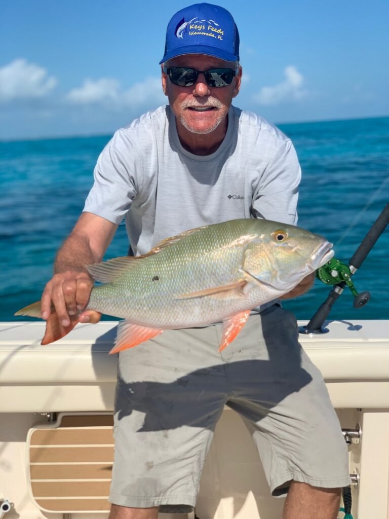 Angler in Keys Feeds hat holding a mutton snapper caught offshore using live bait enhanced with premium fish food